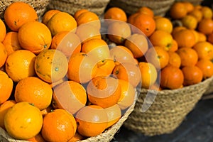 Pile of juicy oranges in wicker baskets on market counter