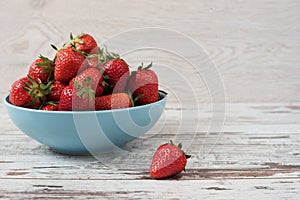 Pile of juicy ripe organic fresh strawberries in a large blue bowl. Light rustic wooden background.