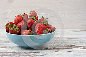 Pile of juicy ripe organic fresh strawberries in a large blue bowl. Light rustic wooden background