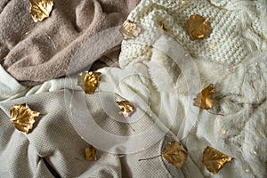 Pile of knitted clothes with autumn gold leaves, warm background, knitwear, space for text, Autumn winter concept.