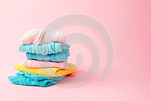 Pile of knitted sweaters and cozy scarves on pink background with copy space, Stack of clothes