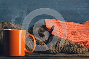 Pile of knitted warm clothes and cup mug tea on wooden background, sweaters, knitwear