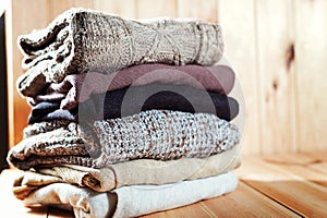 Pile of knitted winter clothes on wooden background, sweaters, space for text