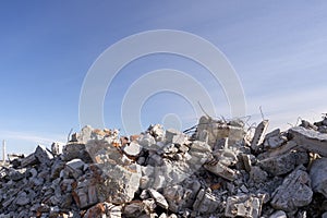 A pile of large gray concrete fragments with protruding fittings against a blue cloudy sky. Background