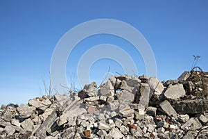 A pile of large gray concrete fragments with protruding fittings against a blue cloudy sky. Background