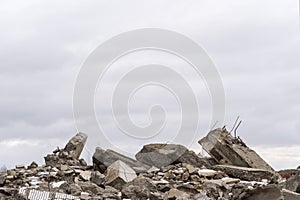 A pile of large gray concrete fragments with protruding fittings against a cloudy sky