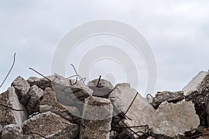 A pile of large gray concrete fragments with protruding fittings against a cloudy sky