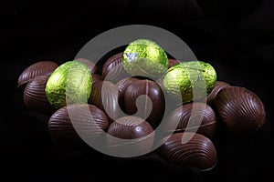 Pile of lime green or yellow foil wrapped & unwrapped chocolate easter eggs against a black background