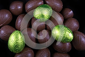 Pile of lime green or yellow foil wrapped & unwrapped chocolate easter eggs against a black background