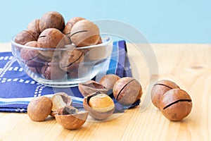 Pile of macadamia nuts in whole kernels and half opened on wooden background with darl blue napkin and translucent bowl. Seeds of