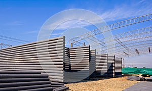 Pile of many metal roof beams for installing on top of large industrial factory building structure in construction site area