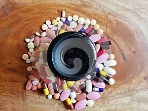 Pile of medicine pills tablets capsules around lens in wooden background