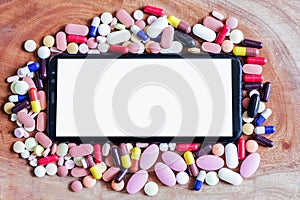 Pile of medicine pills tablets capsules around mobile phone in wooden background
