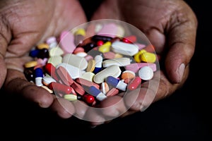 Pile of medicine pills tablets capsules in a both hands in black background