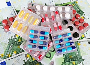 Pile of medicines in blister packs with a variety of  colorful pills and capsules. One hundred Euro banknotes in the background.