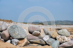 A pile of mixed colourful rocks sit on a golden sandy beach