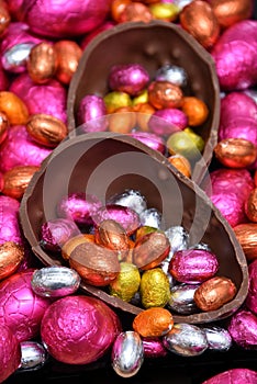 Pile of multi colored and different sizes of colourful foil wrapped chocolate easter eggs in pink, red, gold, silver and orange.