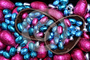 Pile of multi colored and different sizes of colourful foil wrapped chocolate easter eggs in pink, red, silver and blue.