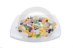 A pile of multi-colored pills on a white plate symbolizing food. Vitamins on a white isolated background. Different