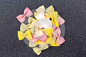 Pile of multicolored green yellow and red bowtie pasta on a black cutting board top down