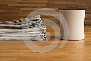 A pile of Newspapers and a Cup on a wooden table