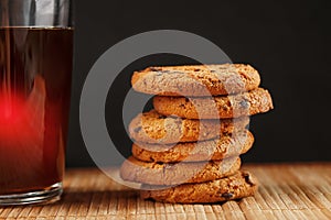 A pile of oatmeal cookies with chocolate chips and a mug of fragrant black hot tea in on a bamboo substrate, on a dark background