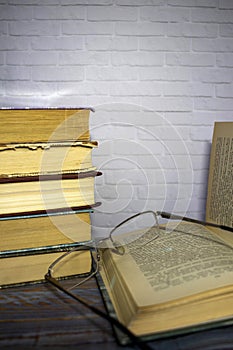Pile of old books with reading glasses on desk