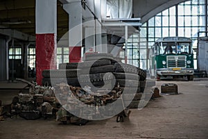 A pile of old car parts and tires in a large garage building with a green bus on a bokeh background