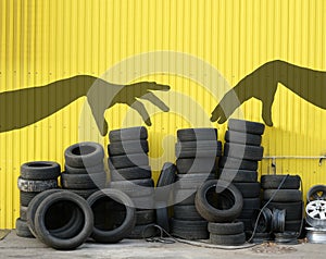 Pile of old car tires against yellow wall of tire service, season changes, shadow of hands choose tyres, copy space