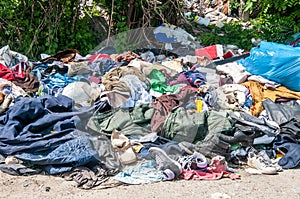 Pile of old clothes and shoes dumped on the grass as junk and garbage, littering and polluting the environment