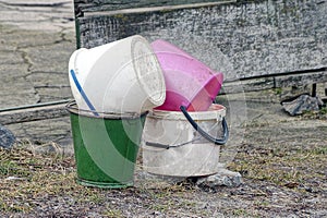 A pile of old colored plastic and metal buckets stand on the ground