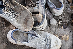 A pile of old dirty shoes lies on the ground. Worn out shoes. Poverty and misery concept