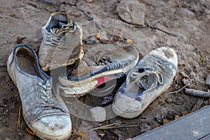 A pile of old dirty shoes lies on the ground. Worn out shoes. Poverty and misery concept