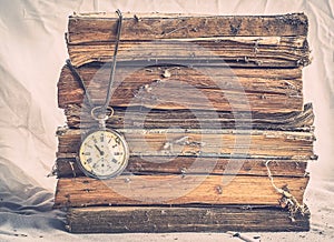 Pile of old dusty books with broken pocket watch on dirty white