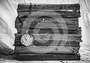 Pile of old dusty books with broken pocket watch on white cloth