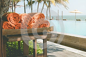 Pile of orange towel put on wooden shelf nearly swimming pool.