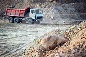 Pile of ore rocks over out of focus background with heavy multi-ton heavy mining truck exporting minerals from open-pit mine.