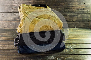 Pile of pants of different colors brown, blue and black on a wooden shelf
