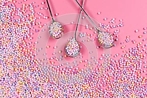 Pile of pastel color sugar balls with spoons on pink background. Mixed colorful candies for sweets decoration. Rainbow colored