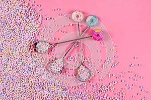 Pile of pastel color sugar balls with spoons on pink background. Mixed colorful candies for sweets decoration. Rainbow colored