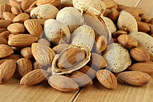 Pile of peeled raw almonds and raw almonds with shells on wooden table. Closeup