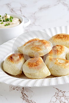 Pile of pierogies with sour cream and spring onions on a platter