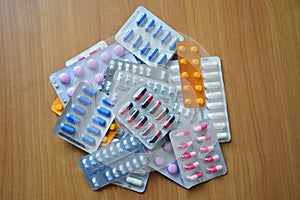 A pile of pills in blister packs. Blister packs full of multi-colored pills. Close up on wooden background.
