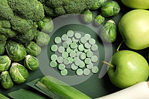 Pile of pills and food on green background, flat lay. Prebiotic supplements