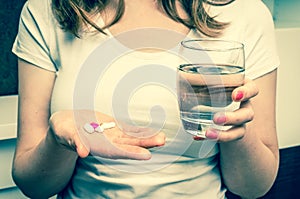 Pile of pills and glass of water in female hands - retro style