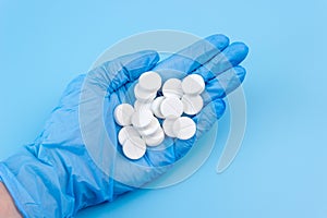 A pile of pills lie in a female hand in a medical glove on a blue background. Health support