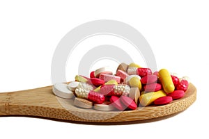 Pile of pills on a wooden spoon on a white background