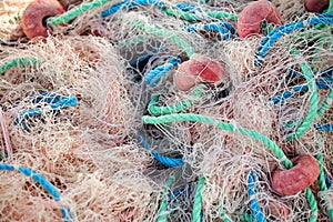 Pile of pink fishing net with blue and green ropes and red buoys on the dock.
