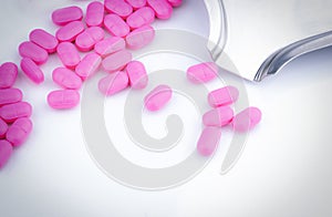 Pile of pink tablets pill on white background near stainless steel drug tray. Ibuprofen 400 mg. Painkiller medicine for headache