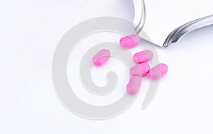 Pile of pink tablets pill on white background near stainless steel drug tray. Norfloxacin 400 mg for treatment cystitis.